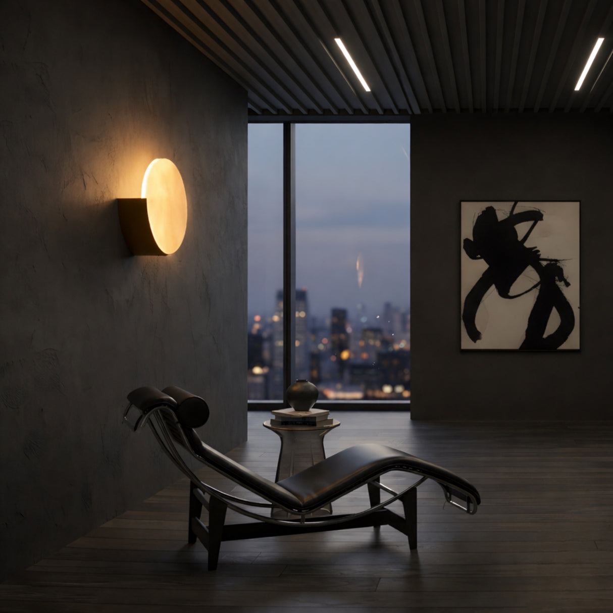 A modern, dimly lit room features a black chaise lounge, small table, abstract art, a large window with a dusk city view, and the Calera LED Large Oval Alabaster Wall Light in Soft White & Brushed Brass.