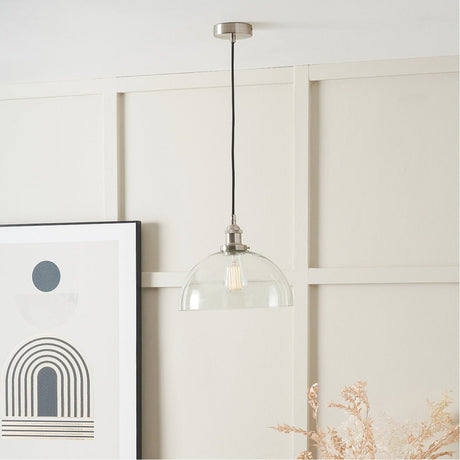 Cecilia dome pendant light, 30cm clear glass shade with antique silver fitting, hanging from a black cord in a room with panelled cream walls.