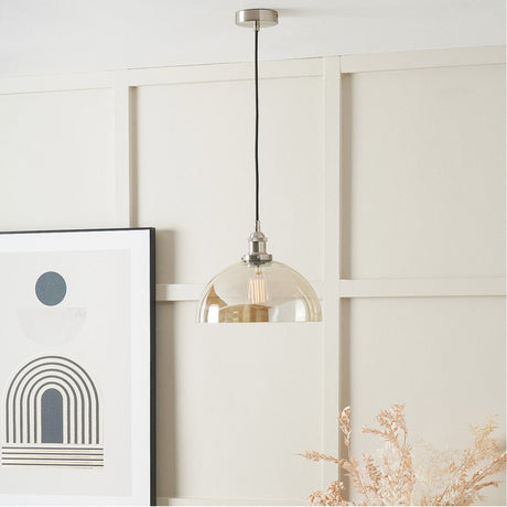 Cecilia pendant light with a 30cm amber glass dome shade and antique silver metal fitting, hung on a black cord above a framed print in a light-panelled room.