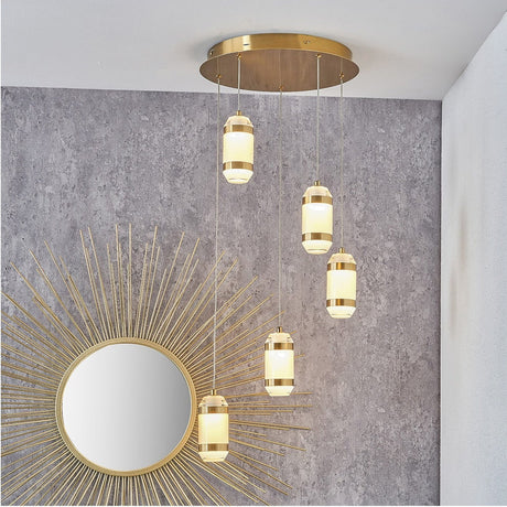 Alondra Gold Iron & White Glass LED Multi Drop Pendant Light with five staggered cylindrical glass shades, shown suspended from a round gold ceiling plate against a grey stone-effect wall.