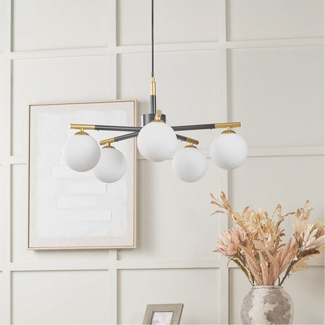 Wanda White Orb & Black Metal 5 Light Pendant - 55cm, a sputnik-style fixture with five glass globe shades on black and brass arms, shown hanging in a neutral-toned living room.