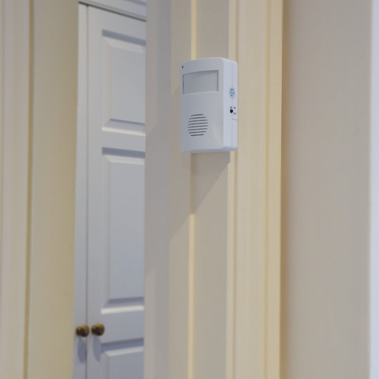 AVSL Mercury motion sensing visitor chime in white ABS housing with PIR sensor window, speaker grille and on/off switch, wall-mounted beside a white door.