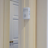AVSL Mercury motion sensing visitor chime in white ABS housing with PIR sensor window, speaker grille and on/off switch, wall-mounted beside a white door.