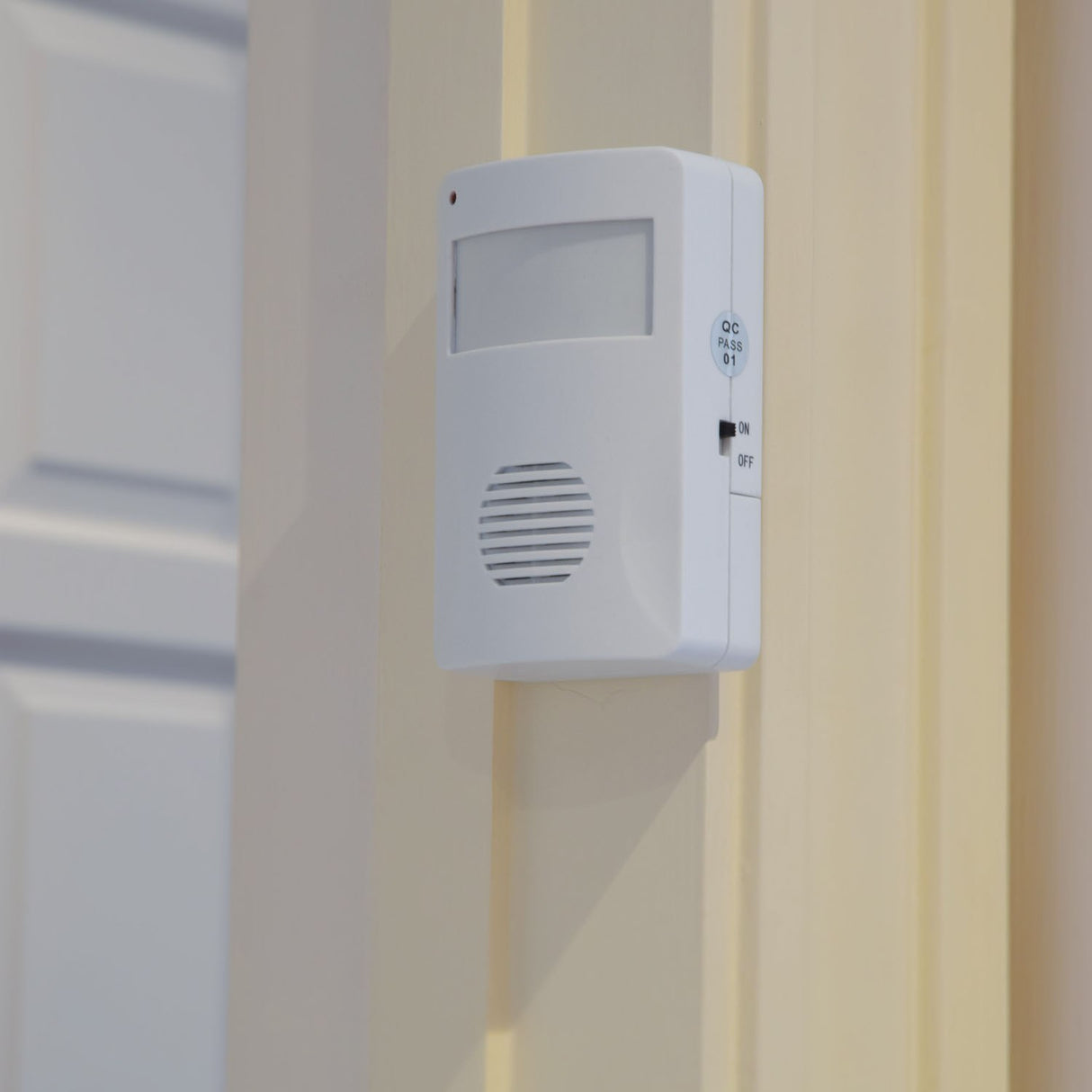 AVSL Mercury motion sensing visitor chime in white ABS housing with PIR sensor, speaker grille and on/off switch, wall-mounted beside a cream door frame.