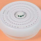 AVSL Mercury heat alarm with white circular vented housing, central thermistor sensor and power button, shown close up on a peach background.