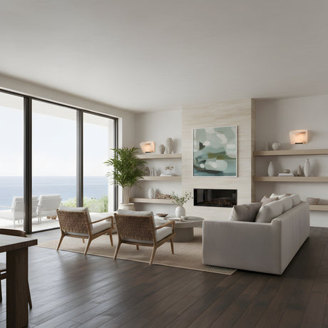 A modern living room with a light sofa, wooden chairs, and coffee table. Large windows show an ocean view. Shelves with decor surround a fireplace under abstract art and the Glorina LED Alabaster Wall Light – Soft White.
