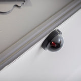 AVSL Mercury dummy dome CCTV camera in black with translucent dome and flashing red LED, mounted beneath a grey moulded ceiling edge against a white wall.