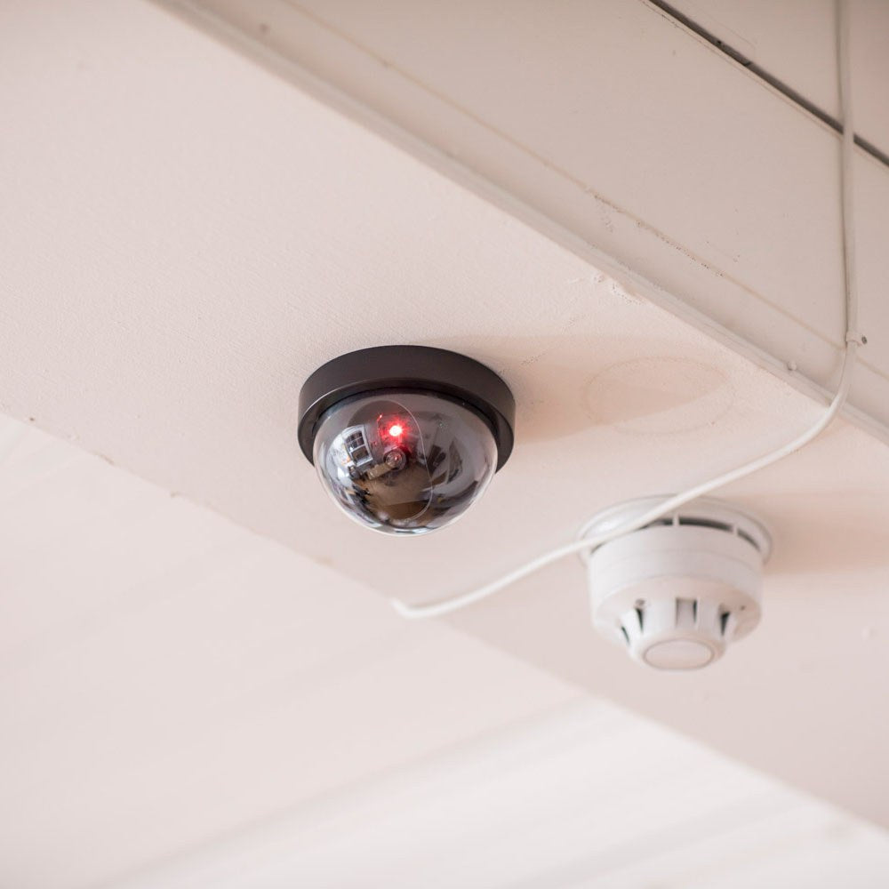 AVSL Mercury dummy dome CCTV camera in black with translucent dome and flashing red LED, ceiling-mounted beside a white smoke detector.