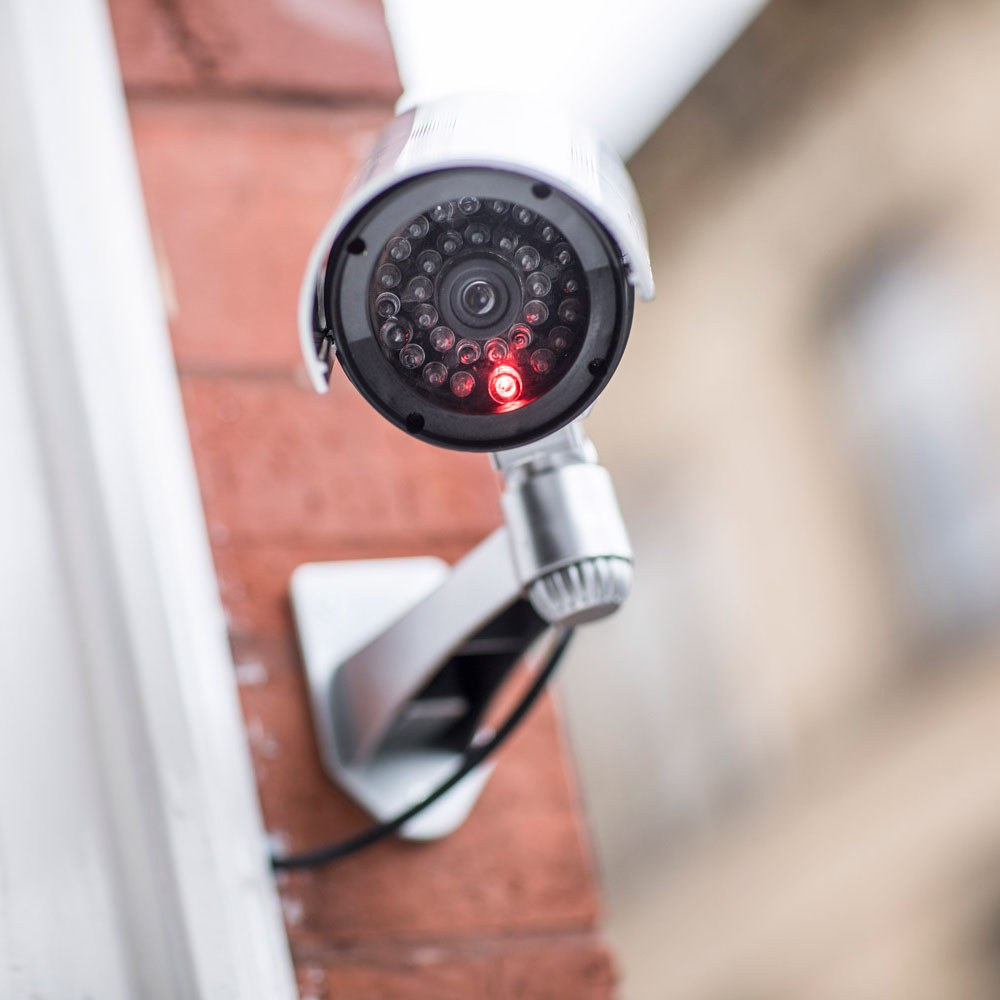 AVSL Mercury dummy IR bullet CCTV camera in white and black plastic with flashing red LED, mock cable and adjustable bracket mounted on a brick wall.
