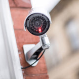 AVSL Mercury dummy IR bullet CCTV camera in white and black plastic with flashing red LED, mock cable and adjustable bracket mounted on a brick wall.