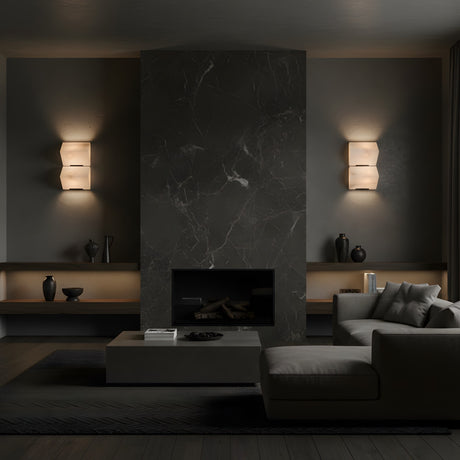 A modern living room with a dark marble fireplace, Glorina LED Small Stacked Alabaster Wall Lights – Soft White on either side, minimalist shelves with vases, a low coffee table, and a gray sectional sofa in moody lighting.