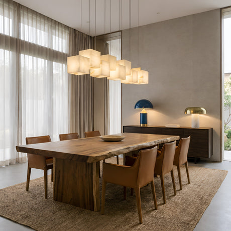A modern dining room with a large wooden table, eight brown leather chairs, a woven rug, and the Elmyra 8 Light Linear Alabaster Bar Pendant Light - Soft White above the table, complemented by a sideboard with two lamps and sheer curtains on tall windows.