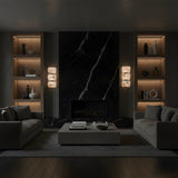 A modern living room features a dark marble fireplace, built-in shelves with soft lighting, beige sofas, a rectangular coffee table, and neutral accessories. The Glorina LED Large Stacked Alabaster Wall Light adds elegance to the minimalist aesthetic.