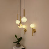 Luceris 1 Light Sphere Alabaster Wall Light in brushed brass, shown illuminated on a wall alongside matching pendant lights in a warm neutral room.