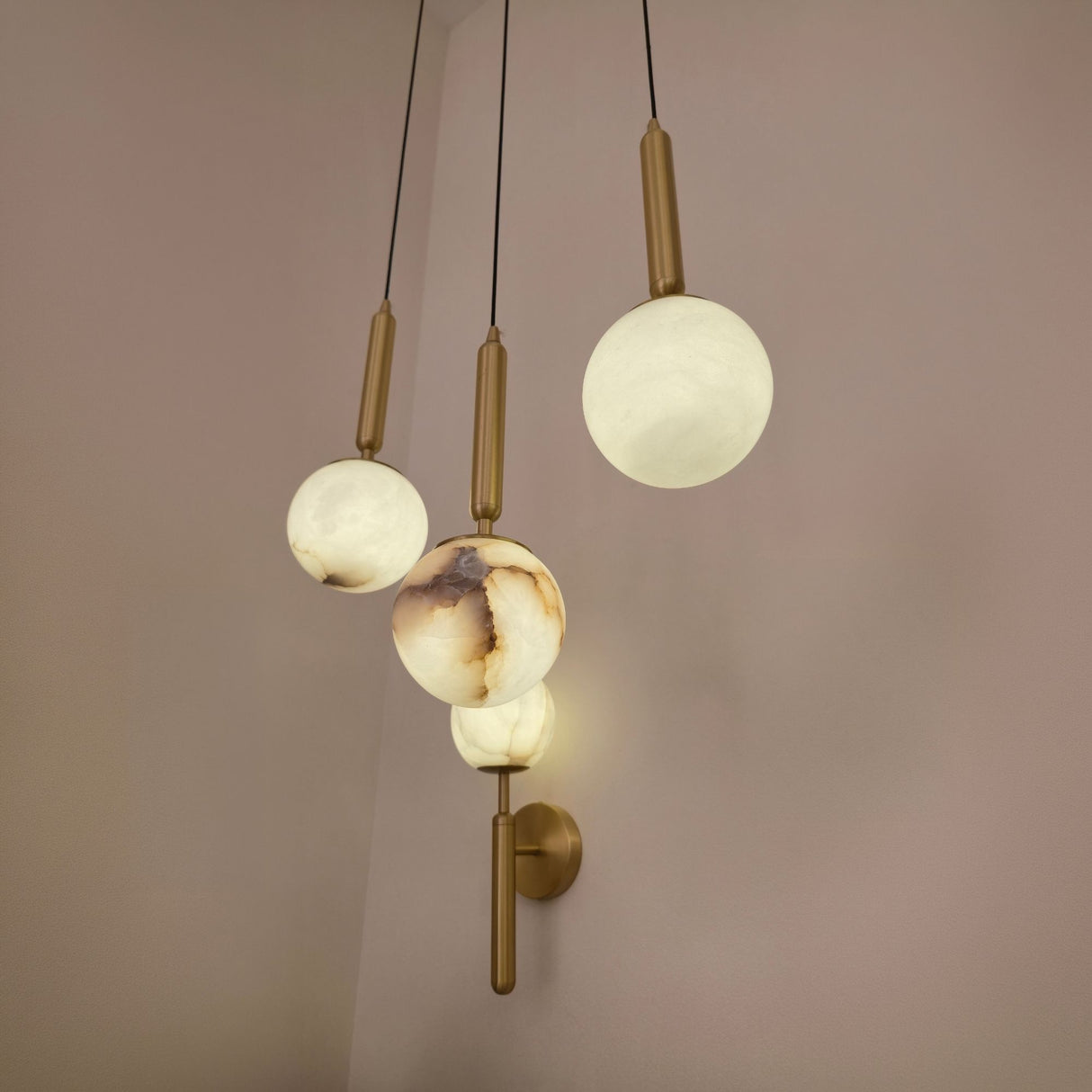 Luceris 1 Light Sphere Alabaster Wall Light in brushed brass, shown alongside matching pendant globes with alabaster spheres in a soft pink-toned room.