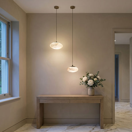 Two Solenne alabaster orb pendant lights with matt black caps hang above a wooden console table in a hallway with marble flooring.