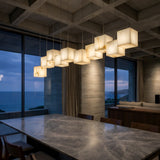Niori Elmyra 10 Light Linear Alabaster Suspension in soft white, staggered cube pendants above a marble dining table in a concrete coffered room.