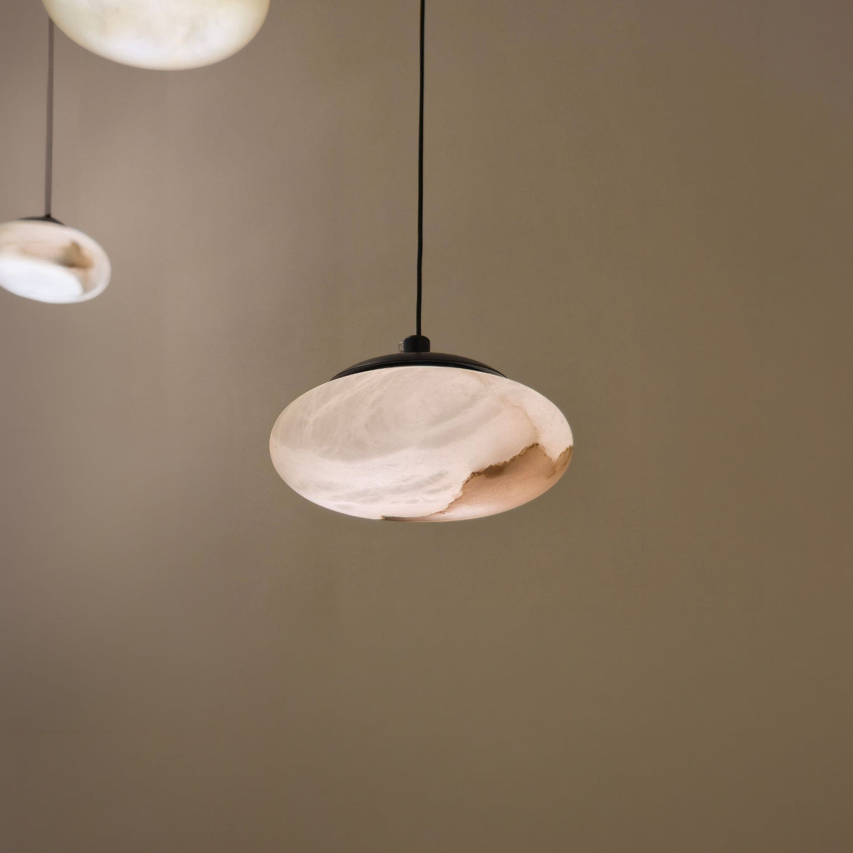 Solenne Small Alabaster Orb Pendant Light in matt black, showing the natural stone shade's veined texture illuminated from within, with matching pendants softly blurred in the background.