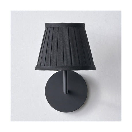 Lyndon black silk mix knife pleated tapered lampshade, 16cm, shown fitted on a matte black wall light against a plain white background.
