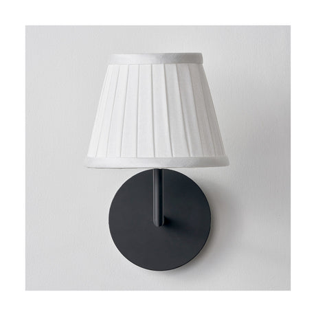 Lyndon ivory silk mix knife pleated tapered lampshade, 16cm, mounted on a black wall light fitting against a plain white background.