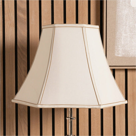 Lyla Cream Silk Mix Bowed Lampshade, 25cm, hexagonal empire shape with tan piped seams, shown on a chrome lamp base against a wood-slat wall.
