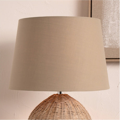 Adelaide Taupe Tapered Cotton Mix Lampshade, 20cm, shown on a wicker-base table lamp against a neutral wall with a framed artwork nearby.