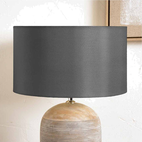 Zara Steel Grey Silk Lined Cylinder Lampshade, 40cm, shown on a wooden ribbed table lamp base against a light neutral wall.
