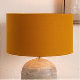 Henry Mustard Handloom Cylinder Lampshade, 40cm, in fabric on a wooden table lamp base, shown against a light neutral wall.