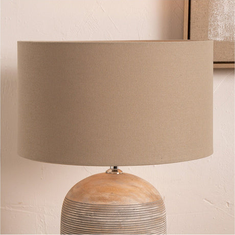 Henry Taupe Handloom Cylinder Lampshade, 35cm, fabric drum shade on a round wooden lamp base, shown against a light wall with a framed picture.