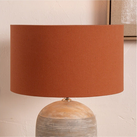 Henry Tobacco Handloom Cylinder Lampshade, 45cm wide in a burnt orange fabric, shown fitted on a textured stoneware table lamp base against a plain wall.
