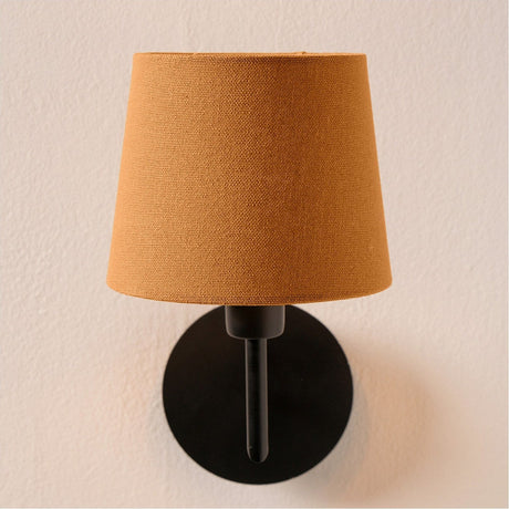 Pelham Mustard Handloom Tapered Candle Clip Lampshade, 15cm, fitted on a black wall sconce with a round backplate, shown against a plain light background.