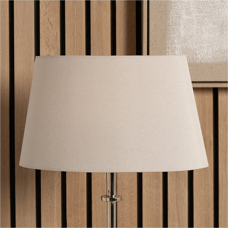 Martha Taupe Oval Silk Mix Tapered Lampshade, 25cm, fabric shade in beige on a chrome table lamp base, set against a wood-slat panelled wall.