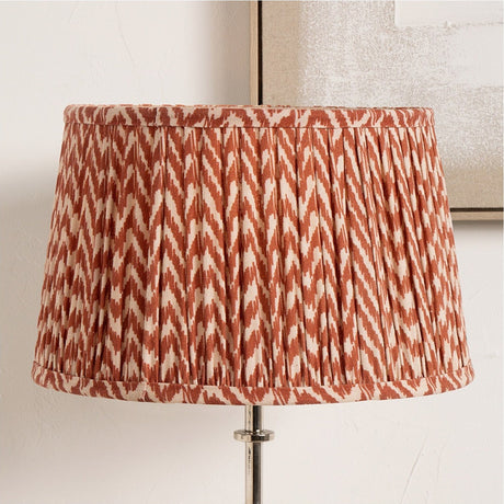 Vienna Red Chevron Pleated Lampshade, 30cm, in fabric with a red and cream zigzag pattern, shown fitted to a floor lamp against a light neutral background.