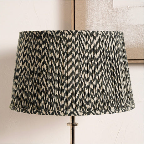 Vienna Black Chevron Pleated Lampshade, 50cm wide, tapered drum shape with pleated fabric in a black and cream zigzag pattern, shown fitted on a lamp base indoors.
