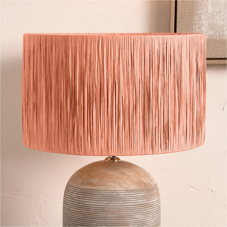 Tilia Apricot Raffia Cylinder Lampshade, 30cm wide, textured drum shade in apricot orange, shown on a rounded wooden lamp base against a neutral wall.