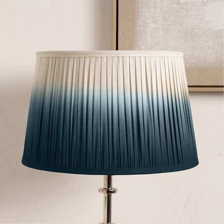 Tapered pleated lampshade, 20cm, in fabric with a blue ombre effect fading to cream at the top, shown on a chrome lamp base against a neutral wall.