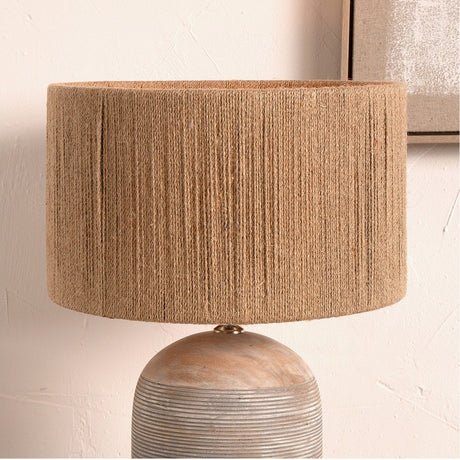 Issa Rope Cylinder Lampshade in natural woven jute, 35cm wide, shown fitted on a textured stoneware table lamp base against a light wall.