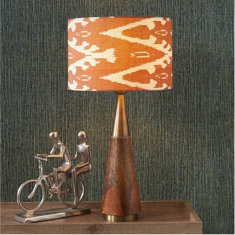 Lars Cinnamon Ikat Cylinder Lampshade, 40cm, in orange and cream patterned fabric, shown atop a wood and brass table lamp base in a home setting.