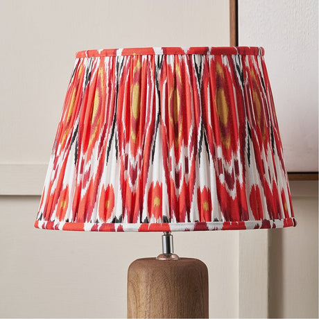 Izara Red Ikat Pleated Tapered Lampshade in 30cm, fabric with red, white and black ikat pattern, shown on a wooden table lamp base.