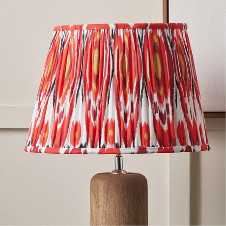 Izara Red Ikat Pleated Tapered Lampshade, 45cm, in red and white ikat-patterned fabric with pleated finish, shown on a wooden table lamp base.