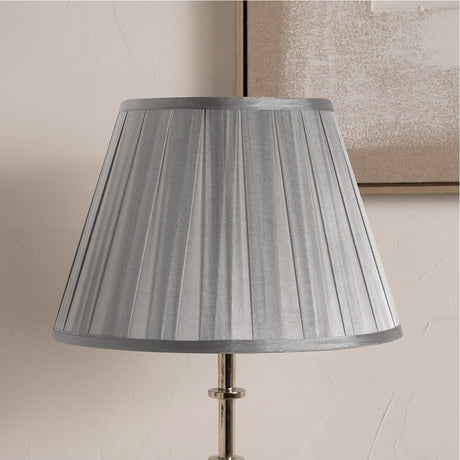 Maya Steel Grey Silk Box Pleated Tapered Lampshade, 45cm, shown on a chrome lamp base against a neutral wall with a framed picture in the background.