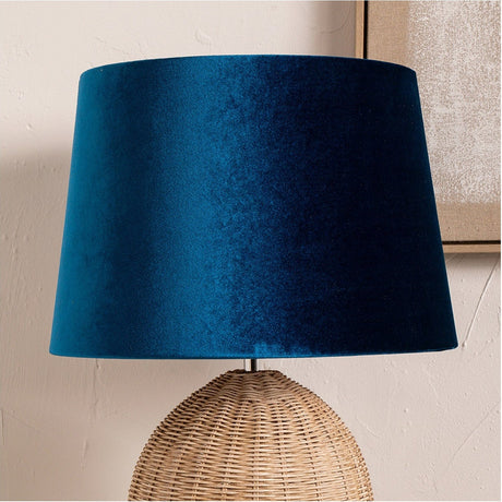 Aida Sapphire Velvet Tapered Lampshade, 50cm, in blue velvet, shown fitted atop a woven rattan table lamp base against a light wall.