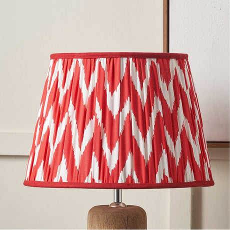 Kamilah Red Chevron Pleated Tapered Lamp Shade, 45cm, in red and white zigzag fabric with red trim, shown fitted on a wooden lamp base.