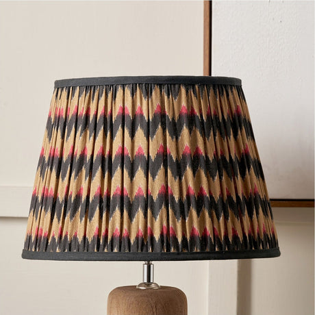 Athira 35cm pleated tapered lamp shade with multi chevron pattern in tan, black and pink, fabric construction with dark trim, shown on a wooden lamp base.