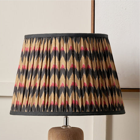 Athira 40cm pleated tapered lamp shade with multi chevron pattern in black, tan and red, black trim, shown on a wooden table lamp base.