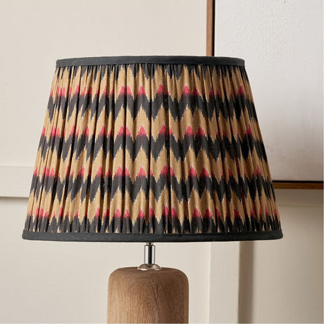 Athira 45cm pleated tapered lamp shade in multi chevron fabric with black trim, shown on a wooden table lamp base against a neutral wall.