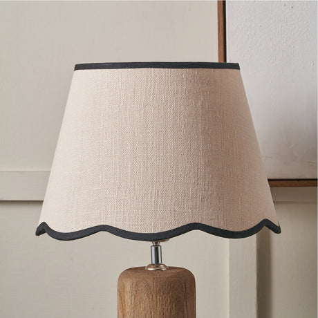 Tabitha tapered lamp shade in cream jute with a scalloped black-trimmed edge, shown on a wooden lamp base against a light background.