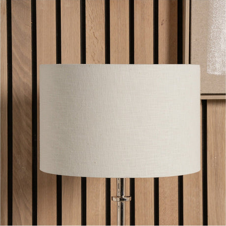 Lino Cream Self Lined Linen Cylinder Lampshade, 25cm, on a lamp base with visible chrome fitting, set against a wood slat panel background.