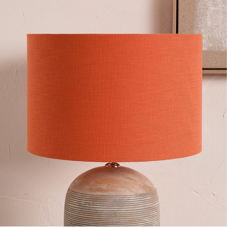 Lino Cinnamon Self Lined Linen Cylinder Lampshade, 40cm, in orange linen fabric, shown fitted on a round ribbed stoneware table lamp base.