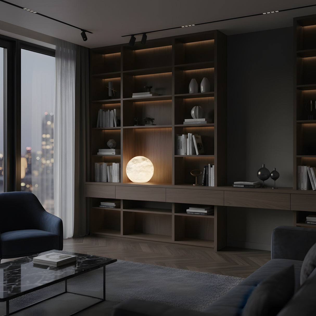 A modern living room with dark wood shelves, books, and decor features the Marvello 1 Light Orb Alabaster Table Lamp in soft white. Large windows reveal a nighttime cityscape, with dark furniture and a marble coffee table completing the look.